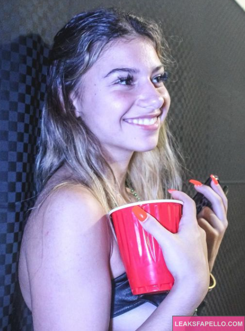 Carlie Sanborn wearing a black bra and holding cup and smiling at camera 