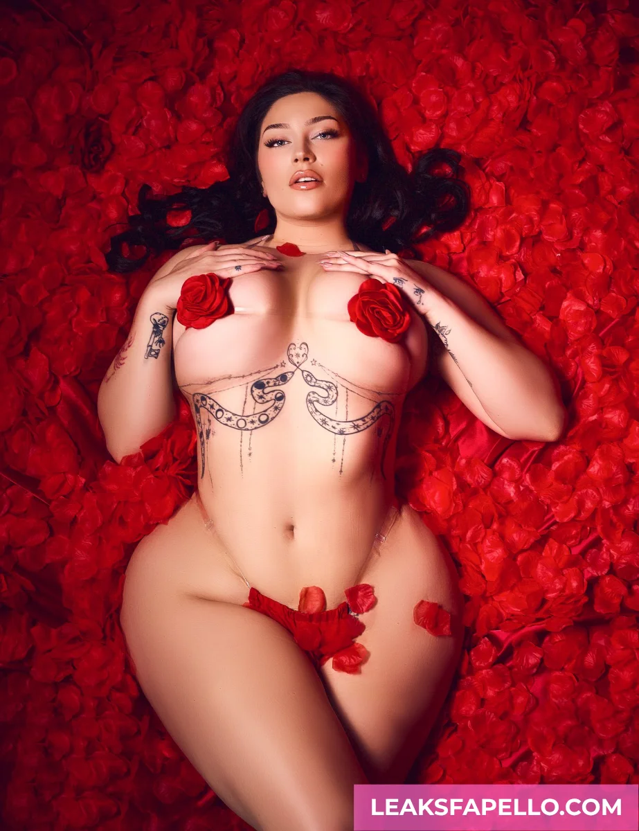 Vivian Taylor, busty MILF tattooed OnlyFans model, lying down on a bed full of rose petals, wearing lingerie made of rose and rose petals