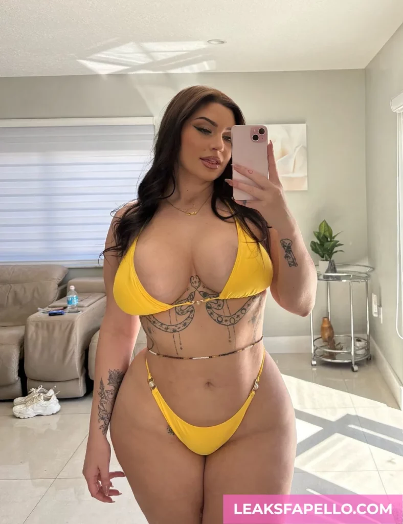 Vivian Taylor, busty MILF tattooed OnlyFans model, wearing a yellow 2 piece bikini, having a mirror shot selfie